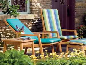 Two wooden reclining chairs with a matching side table and footrest, complemented by colourful cushions.